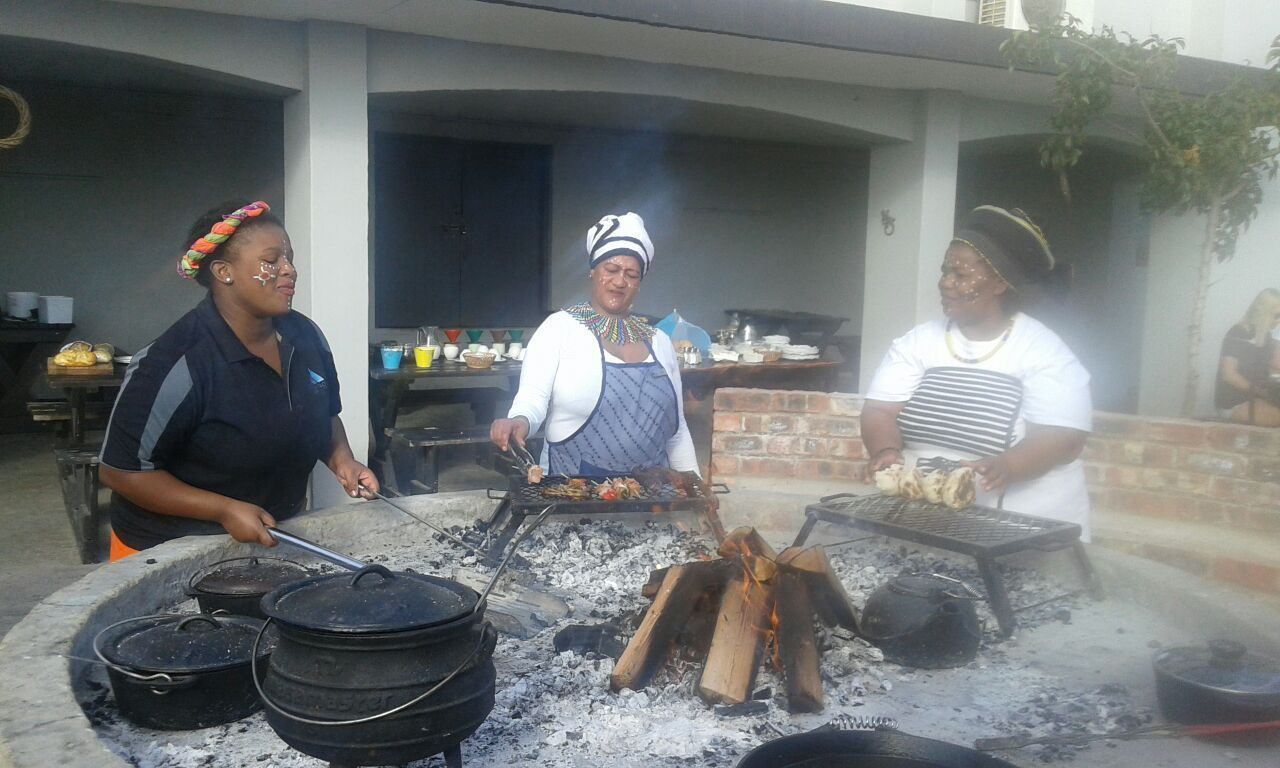 Three people cooking outdoors with a grill and pots.