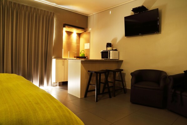A hotel room with a bed, a kitchenette, a TV, and a seating area. - Hotel Portao Diaz (Mossel Bay)