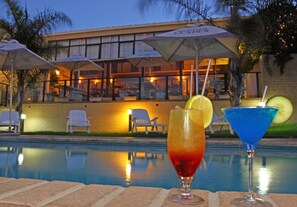 A poolside view with two drinks, a building with outdoor seating, and a brick pool. - Hotel Portao Diaz (Mossel Bay)