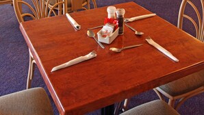 A dining area with wooden tables and chairs, equipped with cutlery and condiments.