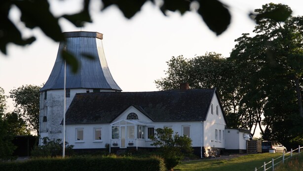 A white house with a distinctive conical roof, surrounded by greenery and a white fence. - Slukefter Kro (Vojens)