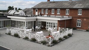 A building with a brick exterior, a covered outdoor seating area with white furniture, and a gravel courtyard. - Slukefter Kro (Vojens)