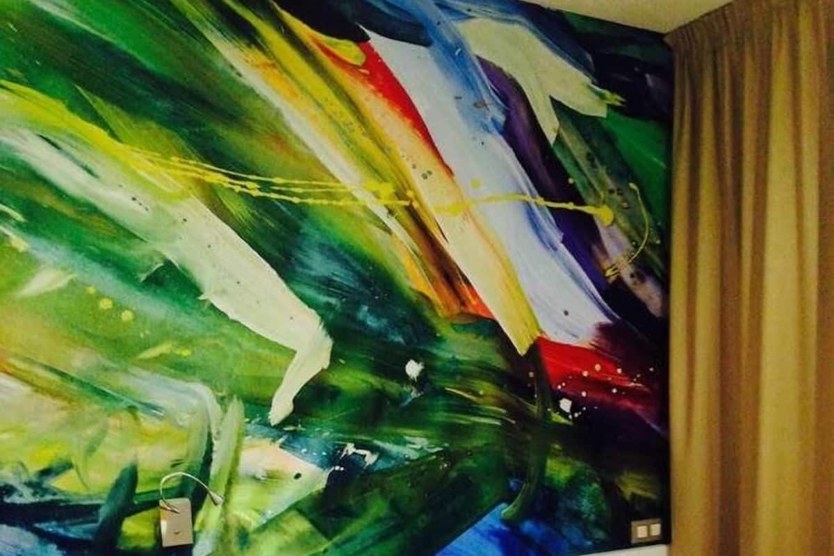 Habitación de hotel con un cuadro abstracto grande en la pared, una cama con ropa blanca, una mesita de noche de madera y una pequeña mesa.