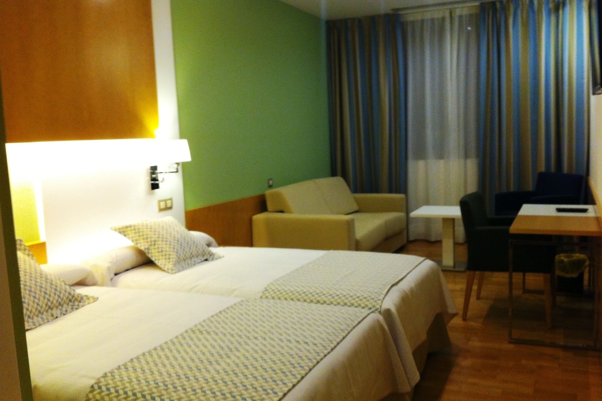 Habitación de hotel con dos camas, una mesita, una silla y un escritorio.