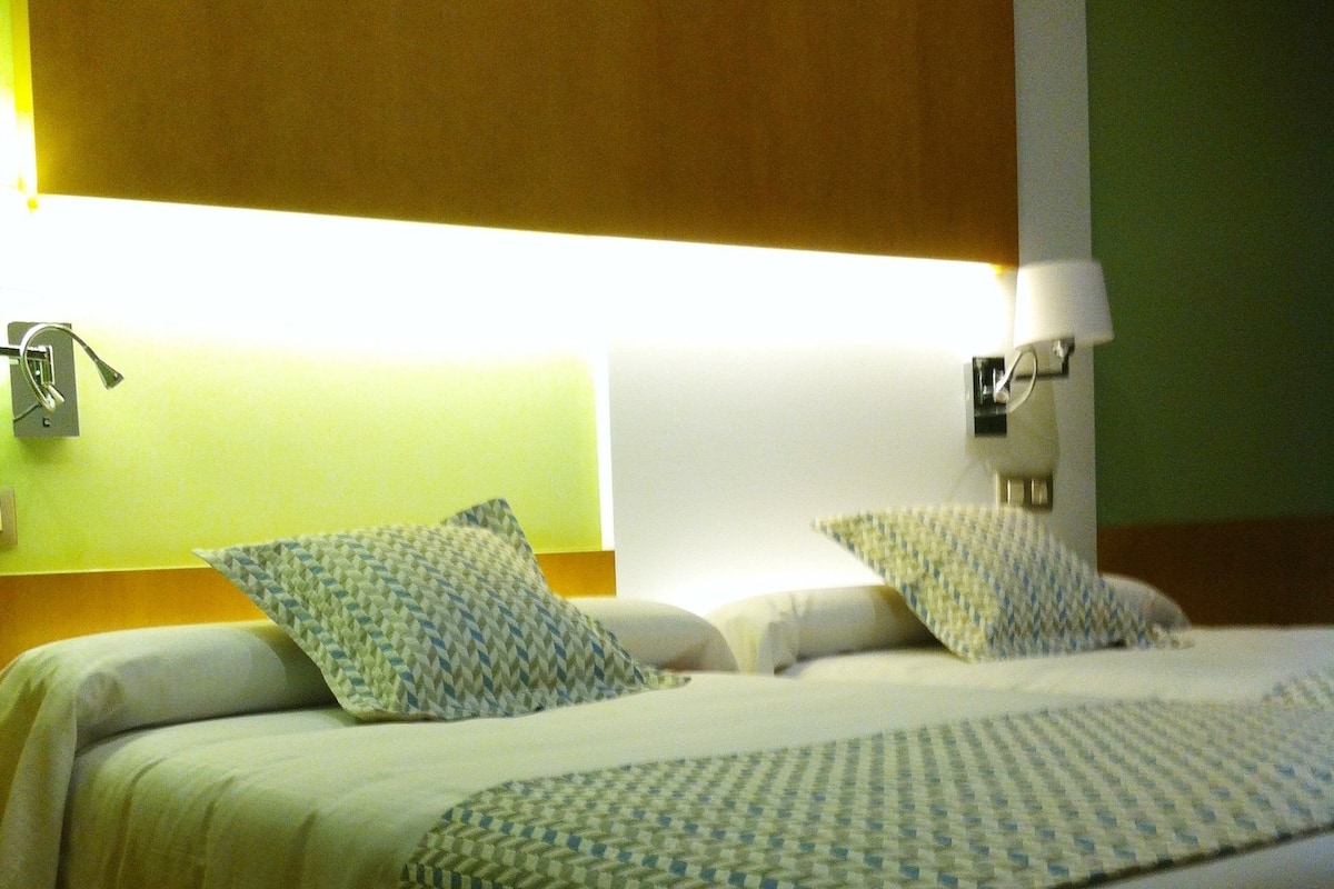 Una habitación de hotel con una cama, dos lámparas de noche y una luz empotrada en la pared.