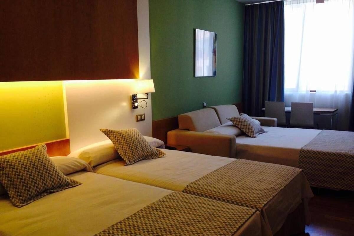 Habitación de hotel con dos camas individuales, un sofá, una mesita y una silla.