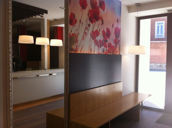 A modern interior with a wooden bench, a wall-mounted painting of red flowers, and a glass partition with a reflection of the room. - Hotel Boutique Museo (Burgos)