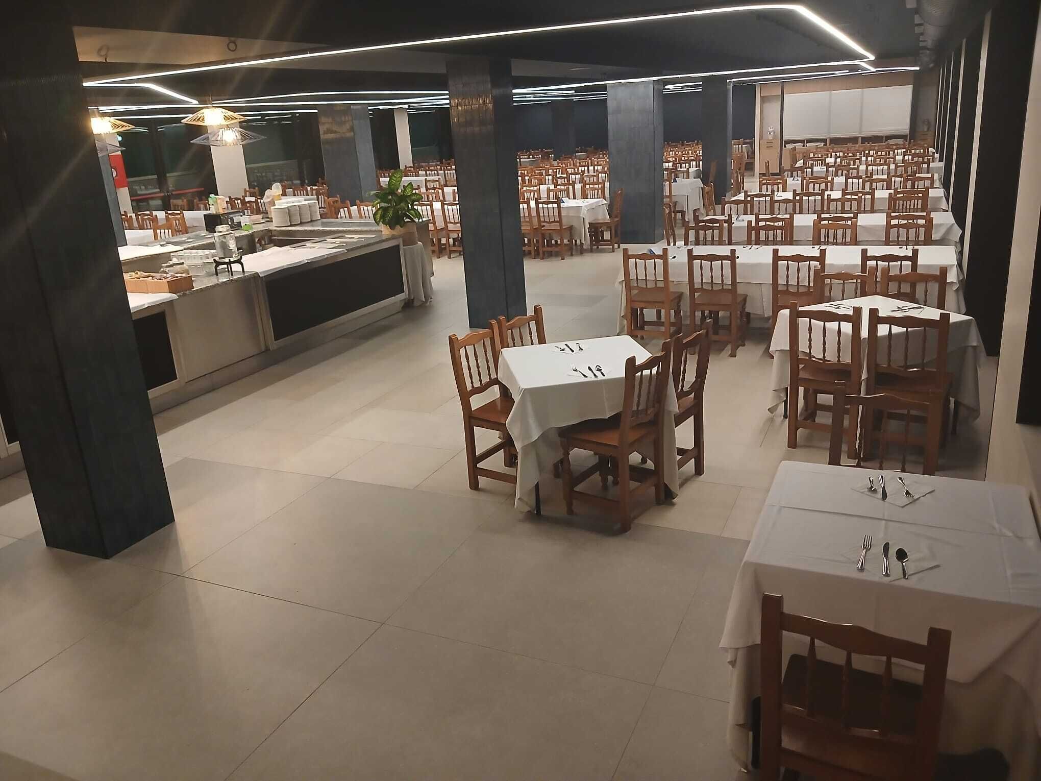 Un comedor amplio con varias mesas y sillas, una barra con mostrador y una ventana grande al fondo.
