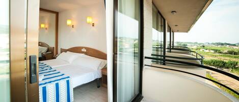 A modern hotel room with a large bed, bedside lamps, and a balcony with a view of the countryside.