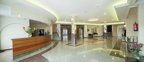 A spacious lobby with a reception desk, a staircase, and a fire extinguisher.