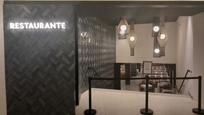 Entrada a un restaurante con una pared de diseño tipo espiga, iluminación colgante moderna y un letrero que dice 'CERADO'.