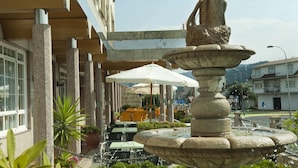 Una fuente de piedra en un patio con mesas al aire libre y un edificio al fondo.