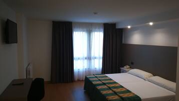 Een hotelkamer met een bed, een bureau, een stoel, een telefoon en een raam met gordijnen.