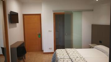 Una camera d'albergo con un letto, una scrivania, una sedia e un televisore appeso al muro.