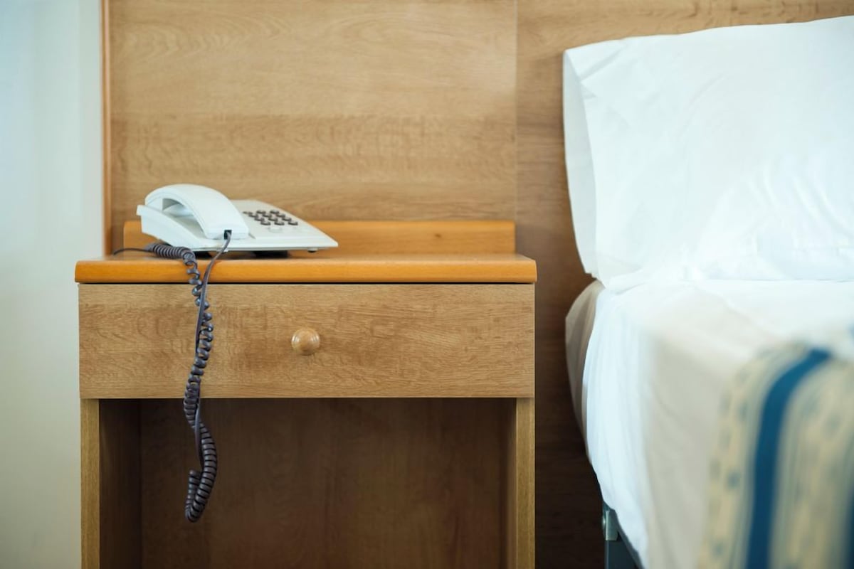 A wooden bedside table with a white telephone and a coiled cord hanging from it.