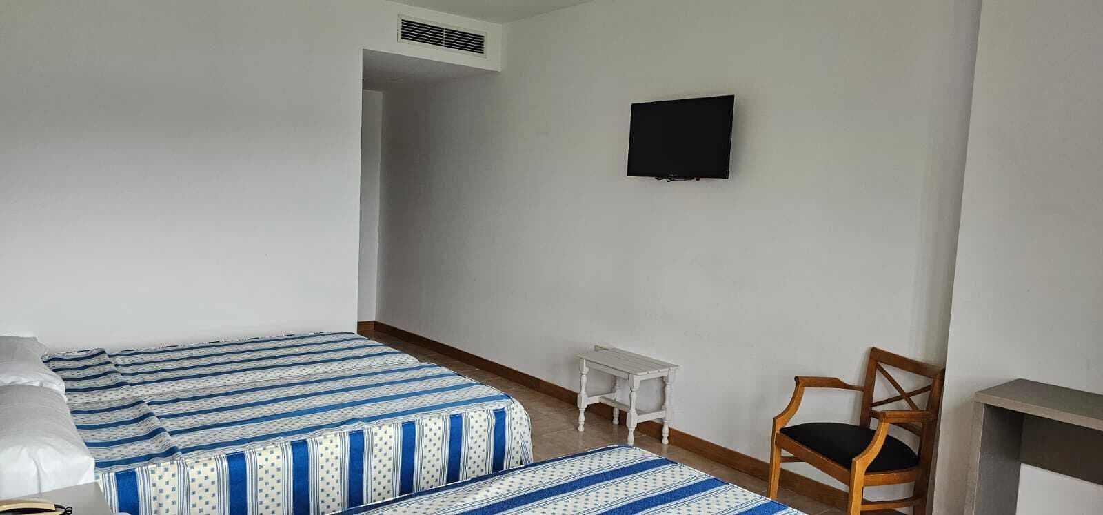 A room with two beds, a TV, a chair, and a small table.