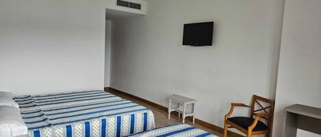 Una habitación con dos camas, televisión, una silla y una mesita.