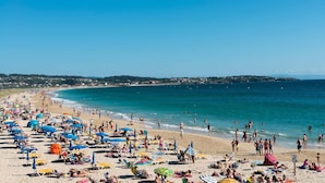 Una playa concurrida, llena de sombrillas y tumbonas.