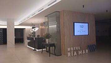 A hotel reception area with a modern design, including a reception desk, a digital display, and a sign indicating the hotel name.