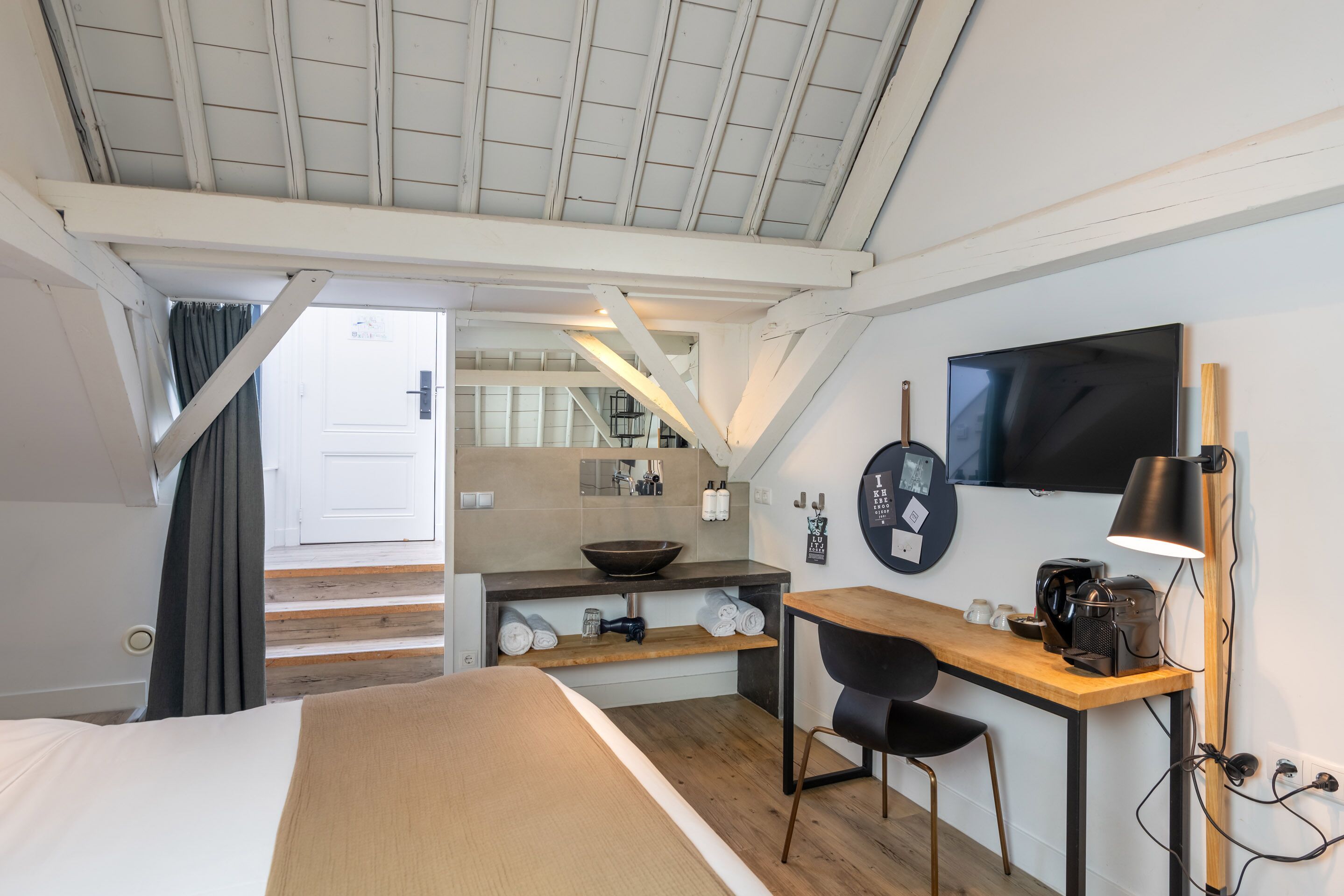 A modern hotel room with a bed, desk, and kitchenette.