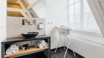 Un baño moderno con un espejo grande, un lavabo negro y una silla blanca cerca de una ventana.