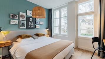 A bedroom with a large bed, a desk, and a window with a view of a house.