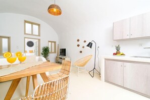 A modern kitchen with a dining area, a hanging light fixture, and a fruit bowl on the counter. - Santorini Suite Home (Santorini)