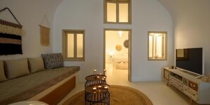 A cozy living room with a sofa, a TV, a fireplace, and a staircase leading to a bedroom. - Santorini Suite Home (Santorini)
