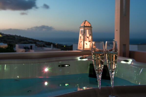 A hot tub with two champagne glasses, a decorative lantern, and a view of the sea and hills.