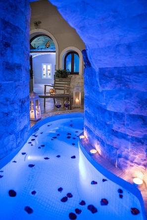 An indoor pool with blue lighting, stone walls, and a bench with a lantern. - Santorini Suite Home (Santorini)