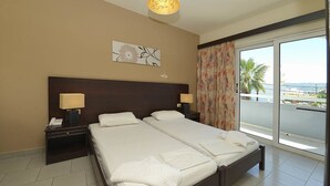 A hotel room with two beds, a nightstand with a lamp, a painting on the wall, and a balcony with a view. - Ialysos City Hotel (Rhodes)