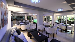 A modern hotel lobby with a dining area, a TV, and a bar. - Ialysos City Hotel (Rhodes)