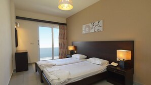 A hotel room with two beds, a large window with a view, a painting on the wall, and a lamp on each nightstand. - Ialysos City Hotel (Rhodes)
