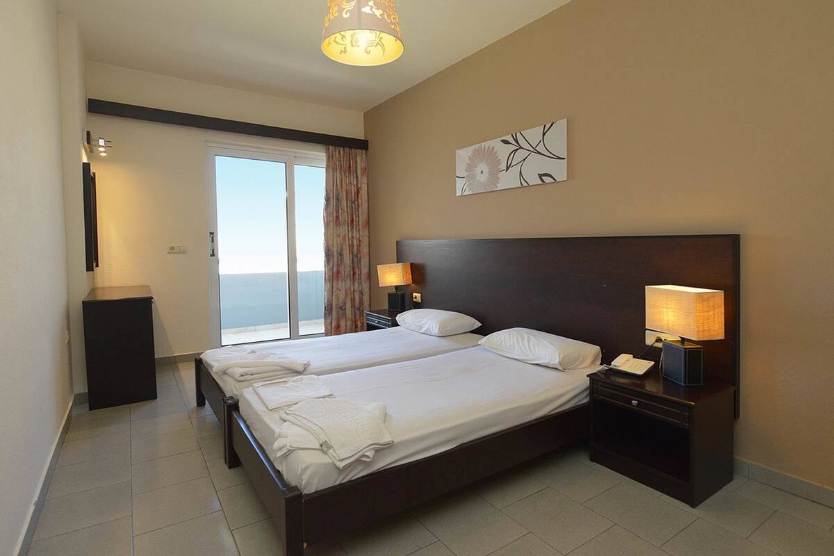 A hotel room with two beds, a large window with a view, a painting on the wall, and a lamp on each nightstand.