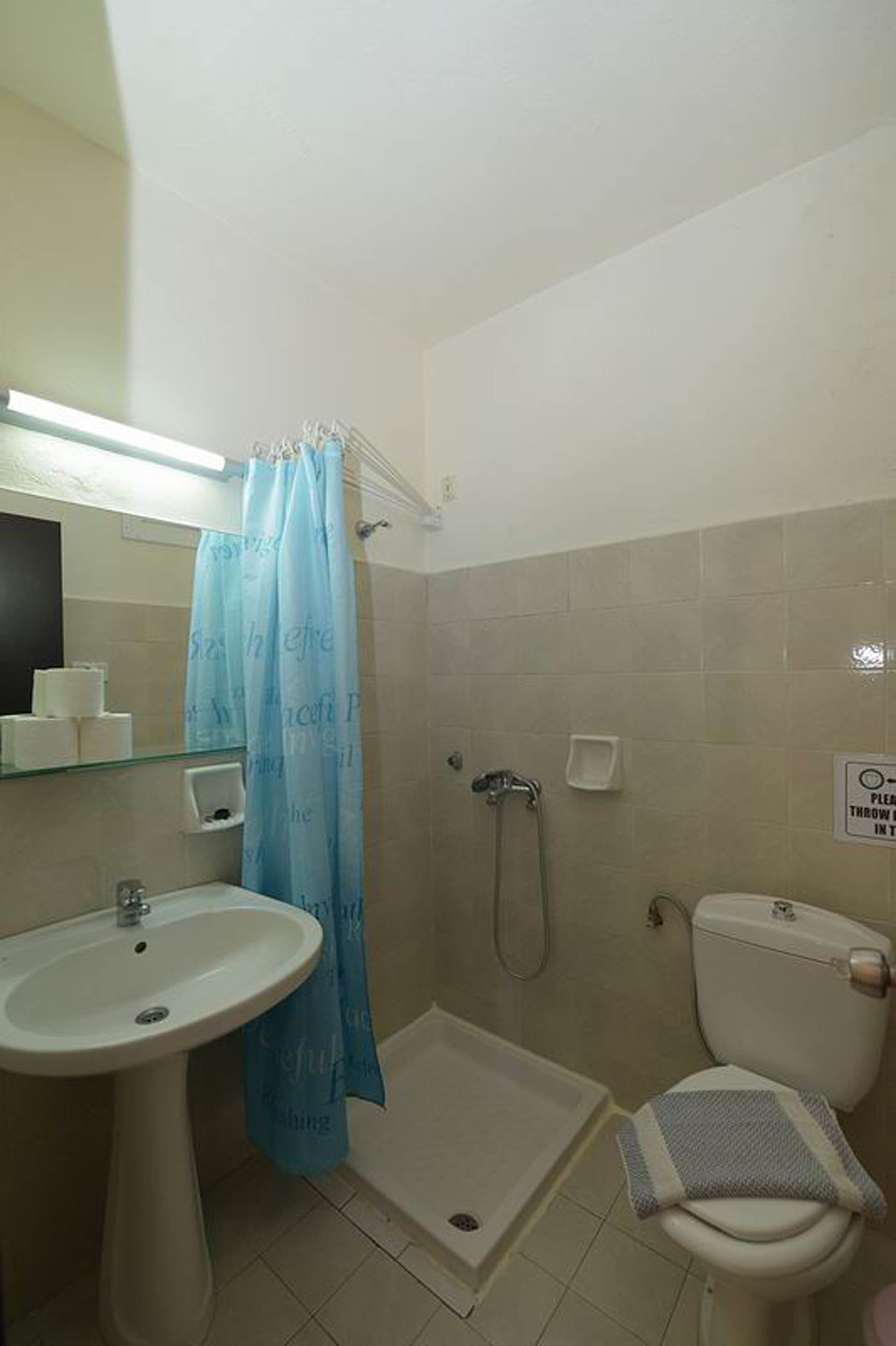 Baño con lavamanos, inodoro, ducha y cortina de vidrio para la ducha.