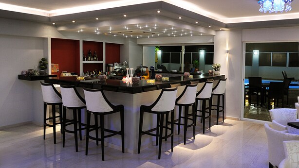 A modern bar area with a curved countertop, multiple bar stools, and a large mirror above the bar. - Ialysos City Hotel (Rhodes)