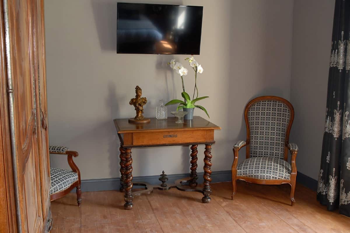 Ein Zimmer mit einem Holztisch, zwei Stühlen, einem an der Wand montierten Fernseher und einer dekorativen Vase mit Blumen.