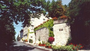 A stone building with a narrow street, surrounded by greenery and flowers. - Hotel La Rocca (Gubbio)