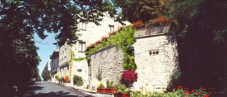 Un edificio de piedra con una calle estrecha, rodeado de vegetación y flores.