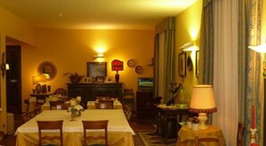 A dining room with a long table, chairs, a fireplace, and a television.