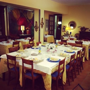 Un comedor con varias mesas dispuestas para comidas, sillas y elementos decorativos como cuadros y lámparas.
