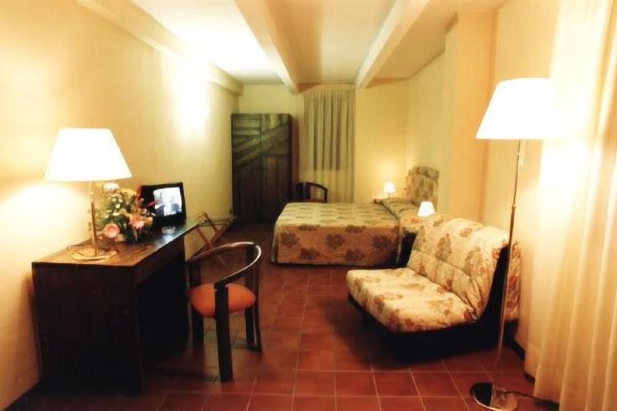 A compact hotel room with a bed, a desk with a computer, a chair, and two bedside lamps.