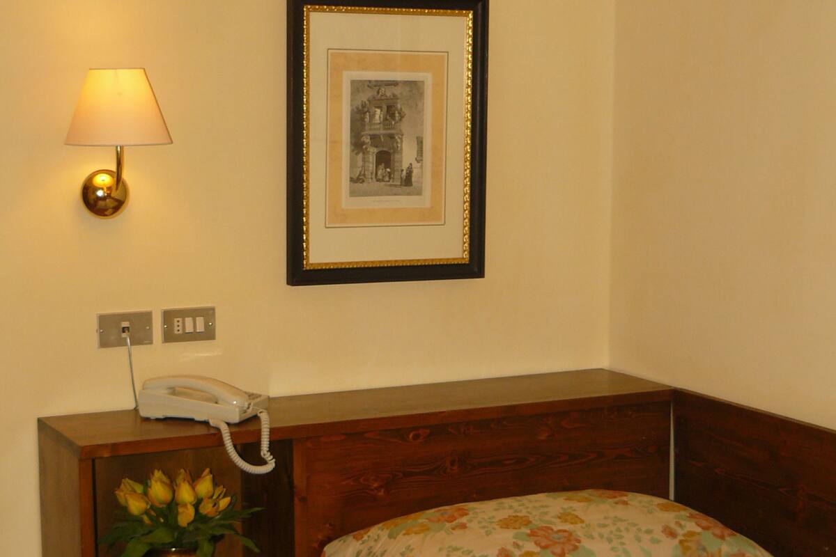 A bedroom with a bed, a bedside table with a lamp, a framed picture, and a telephone.