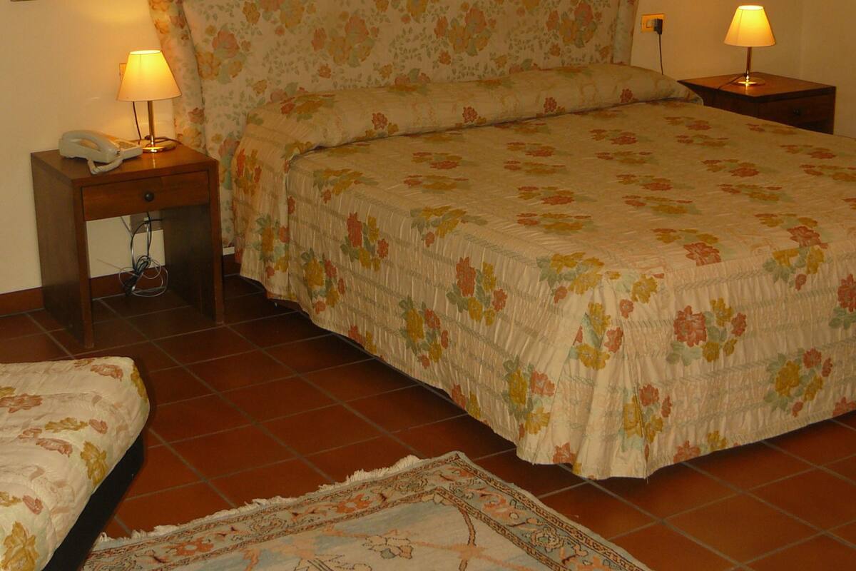 A bedroom with a floral bedspread, two bedside lamps, a nightstand with a phone, and a patterned rug on the floor.
