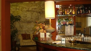 A bar area with a stone wall, a sofa, a lamp, and a variety of bottles on shelves. - Hotel La Rocca (Gubbio)