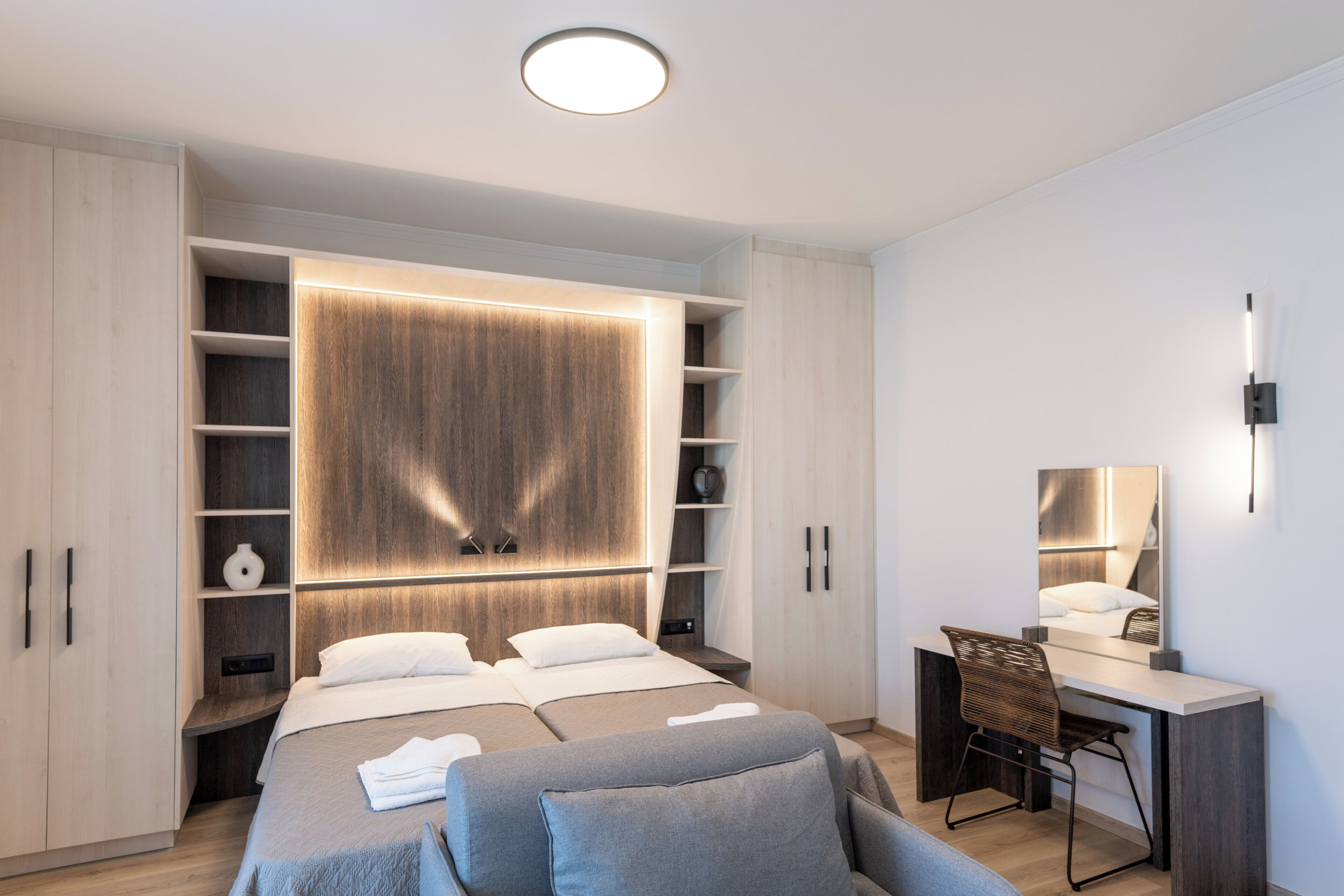 A modern bedroom with two beds, a desk, and built-in shelving.