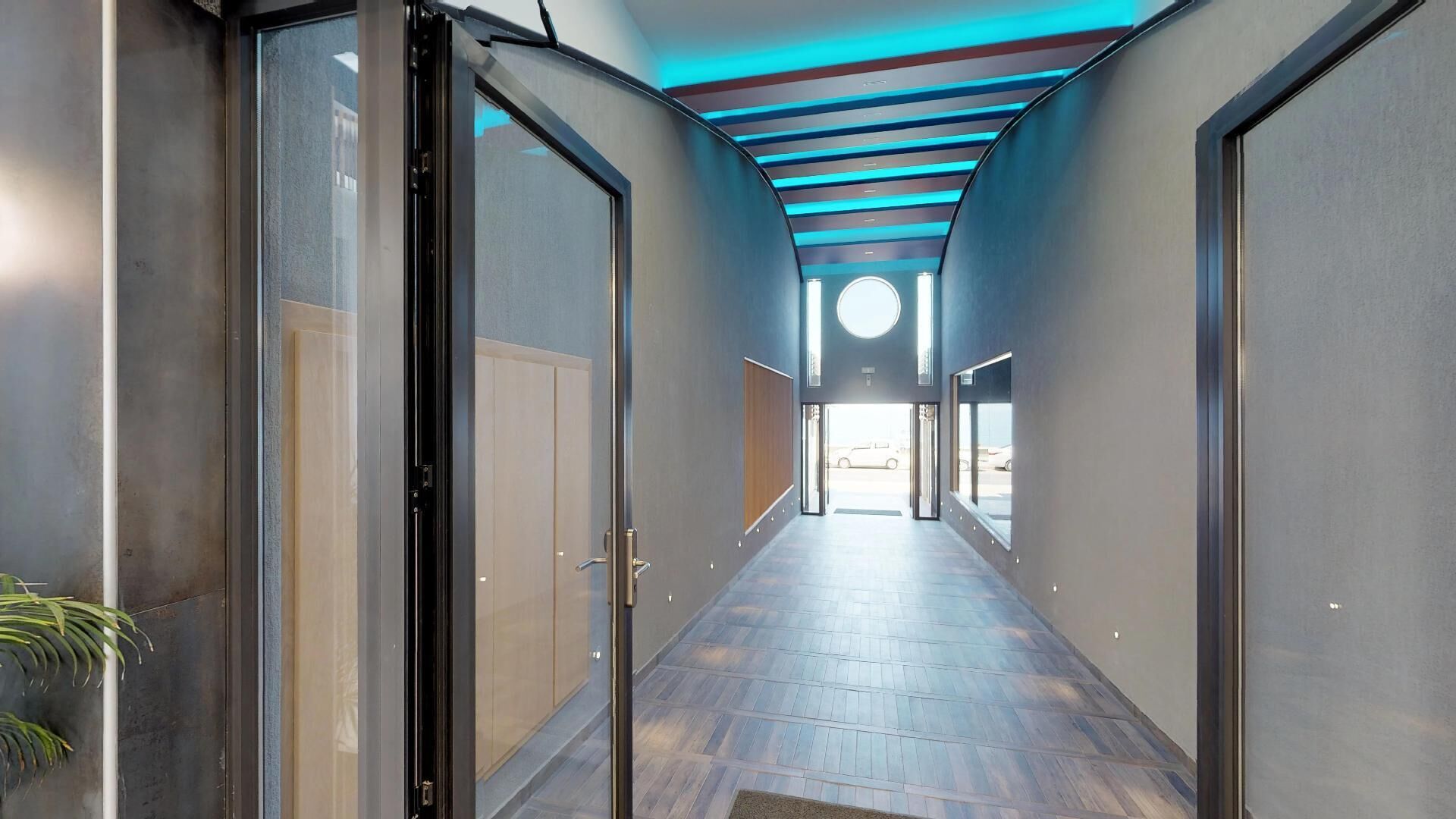 Um corredor moderno com portas de vidro, piso de madeira e teto azul.
