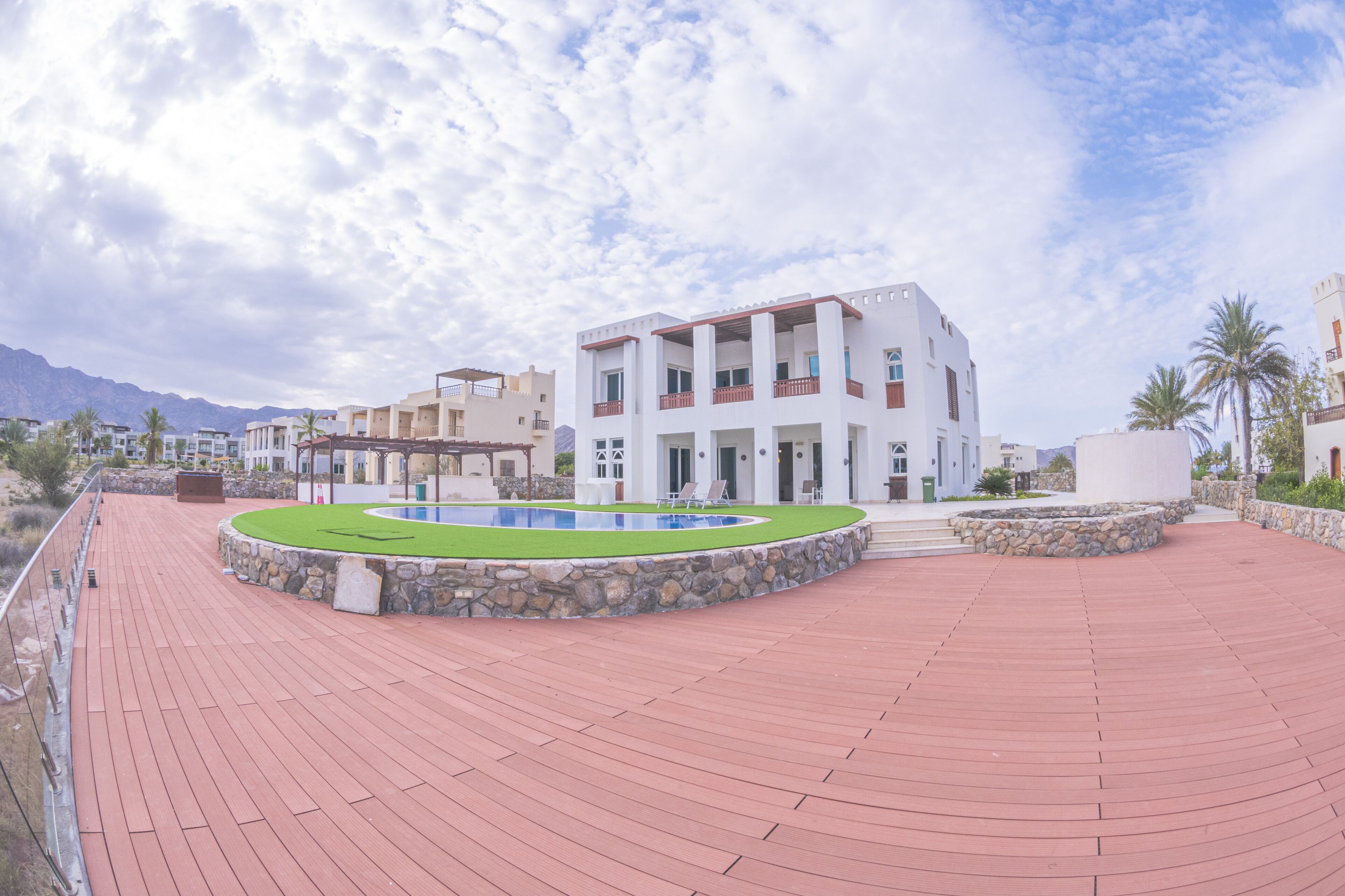 A modern building with a swimming pool, surrounded by a red-tiled deck and stone walls.