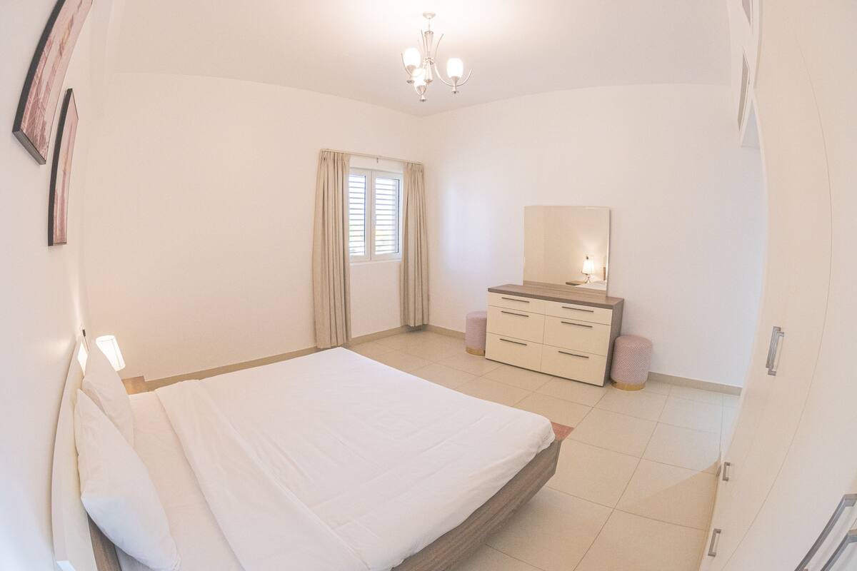 A bedroom with a bed, a dresser, a mirror, and a window with curtains.