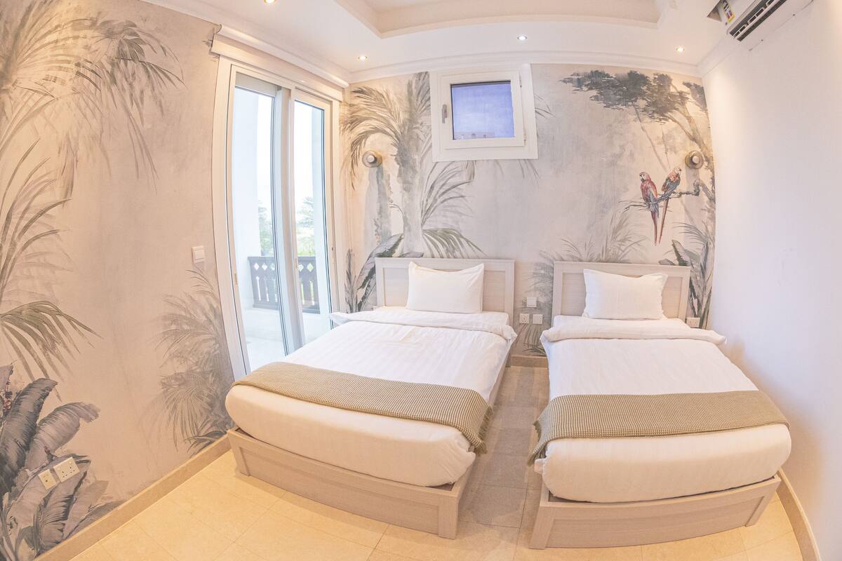 A room with two beds, a large window, and a mural of birds on the wall.